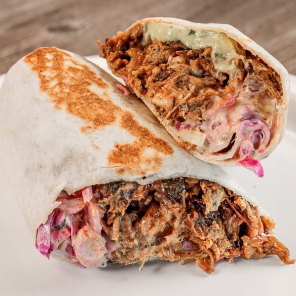 Two halves of a Bone Ends BBQ burrito, revealing pulled pork, coleslaw, and sauce.