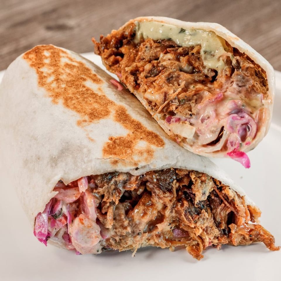 Two halves of a Bone Ends BBQ burrito, revealing pulled pork, coleslaw, and sauce.