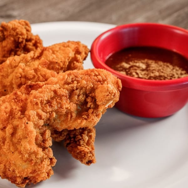 Crispy fried chicken tenders on a white plate with a side of Bone Ends BBQ sauce.