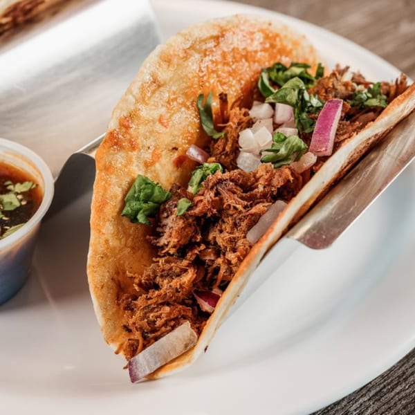 Close-up of a Bone Ends BBQ taco with shredded meat, onions, and cilantro, served with dipping sauce.