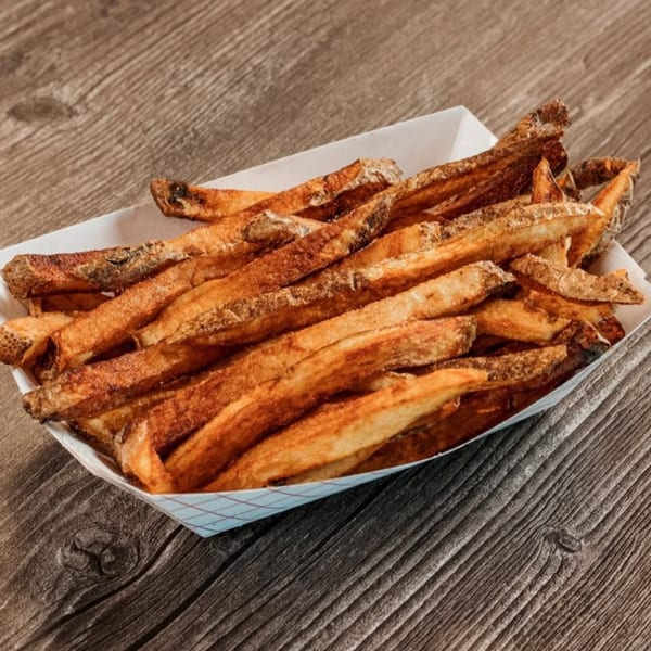 A white paper tray filled with crispy, golden-brown french fries on a rustic wooden table.