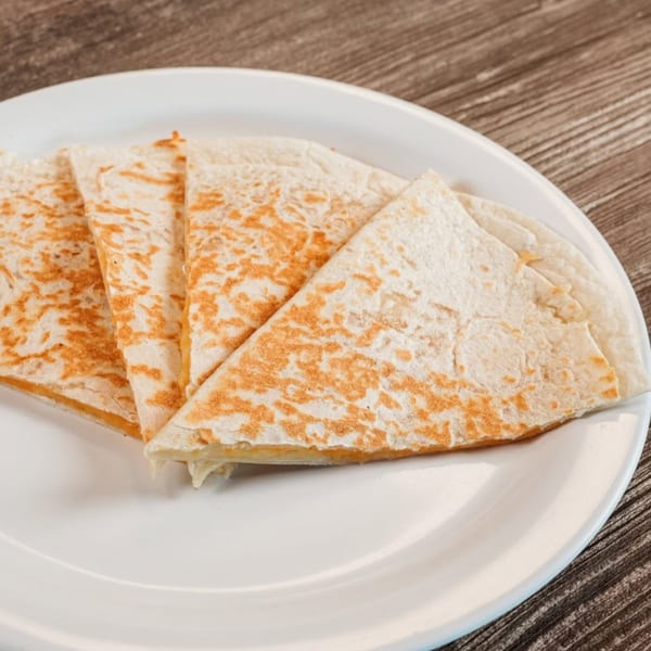 Four triangular quesadilla slices with melted cheese on a white plate, on a wooden table.